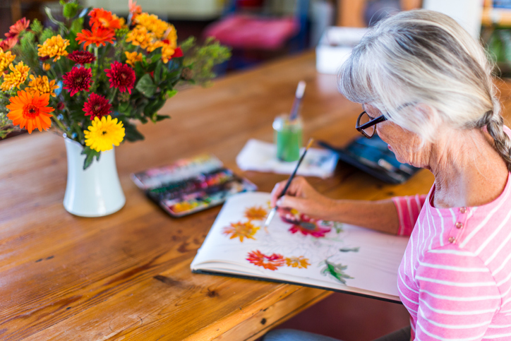 Senior woman painting picture of flowers in a vase at home VENCENDO A ANSIEDADE EM TEMPOS DE COVID-19